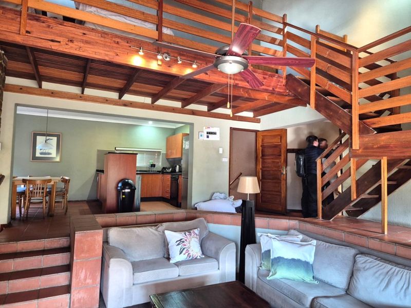Open-plan living area featuring a sunken lounge, wooden staircase leading to a mezzanine loft, and a functional kitchen with built-in cabinetry.