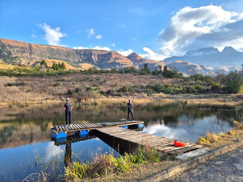 Scenic view of a tranquil pond featuring a wooden jetty set against a backdrop of dramatic mountain ranges.