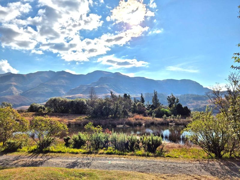 A scenic landscape view featuring a natural pond, surrounding vegetation, and majestic mountain ranges in the background.