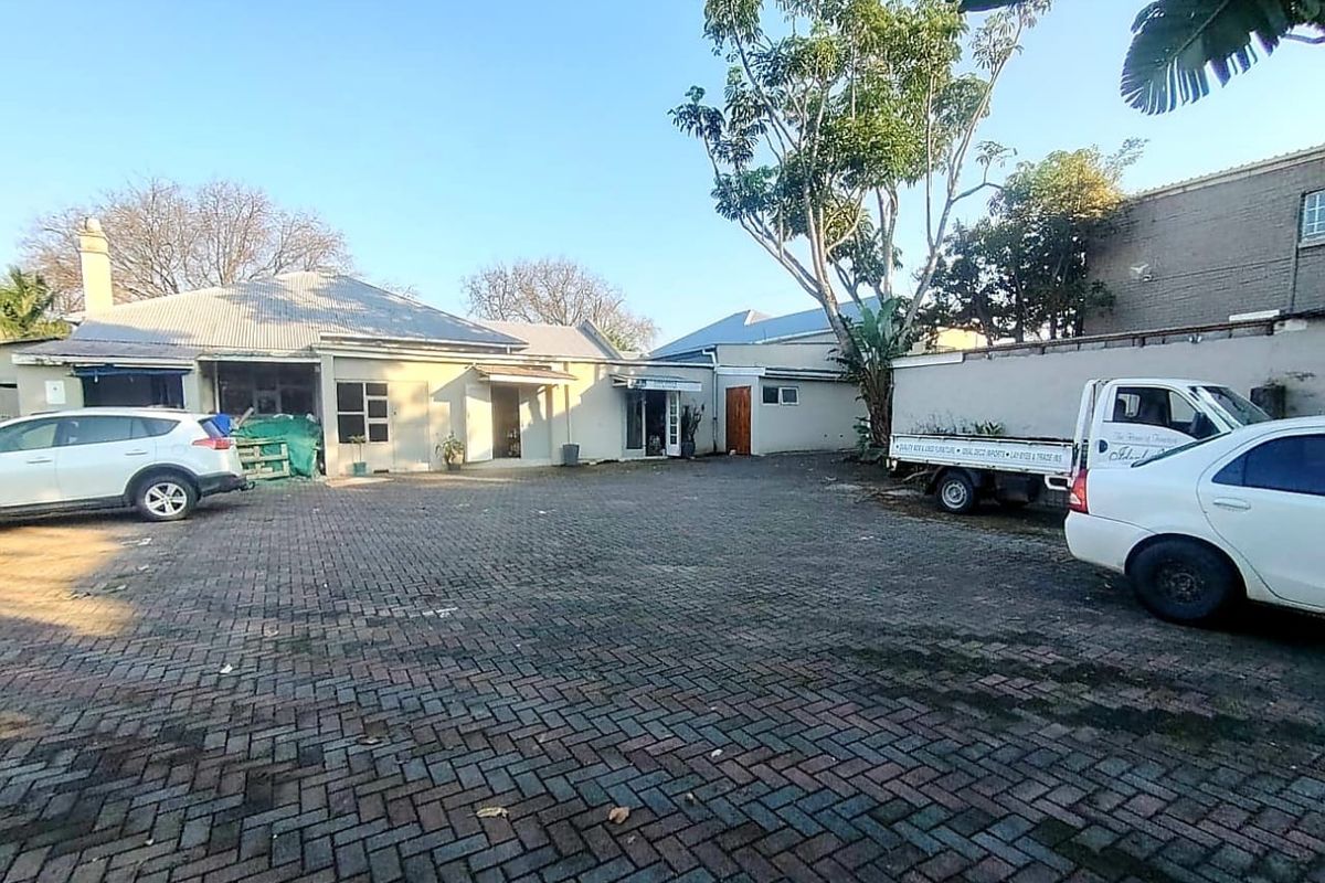 Rear exterior view of the commercial property featuring a large paved parking area, boundary wall, and single-story building structure.