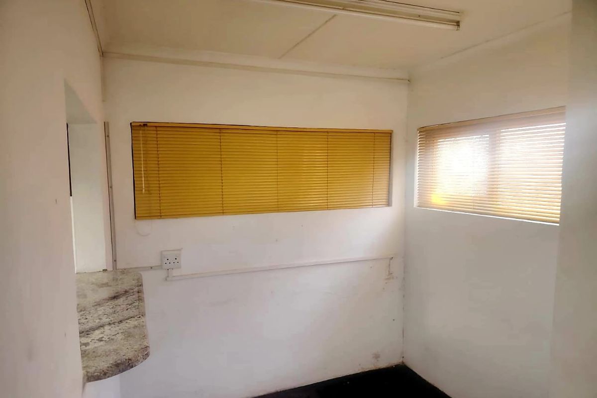 A compact, empty kitchen area featuring a granite countertop, fitted venetian blinds, and basic electrical infrastructure, requiring cosmetic updates to the wall finishes.