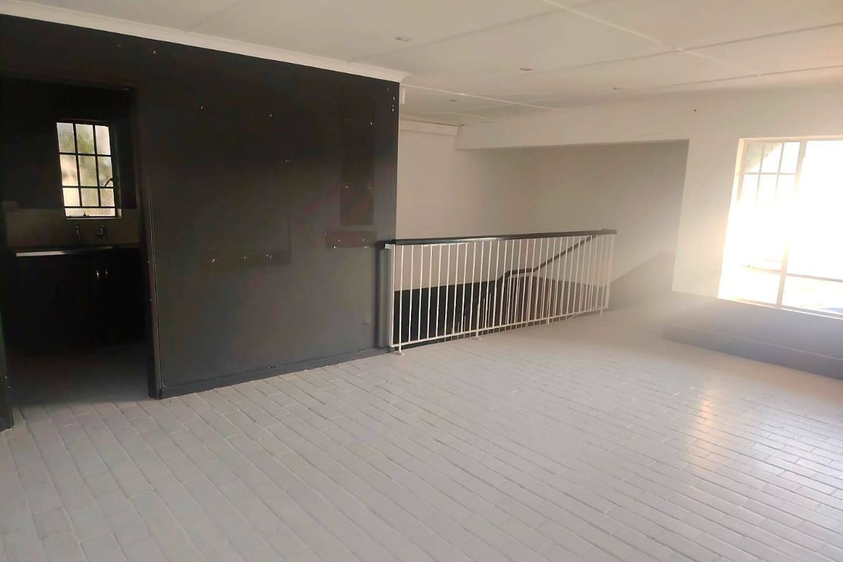An empty, open-plan living area featuring tiled flooring, a metal balustrade, and recessed ceiling lighting, awaiting interior design and finishing touches.