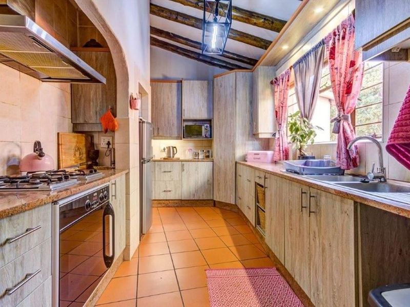 A functional kitchen featuring wood-look cabinetry, gas hob, built-in oven, extractor fan, and exposed timber ceiling beams with tiled flooring.
