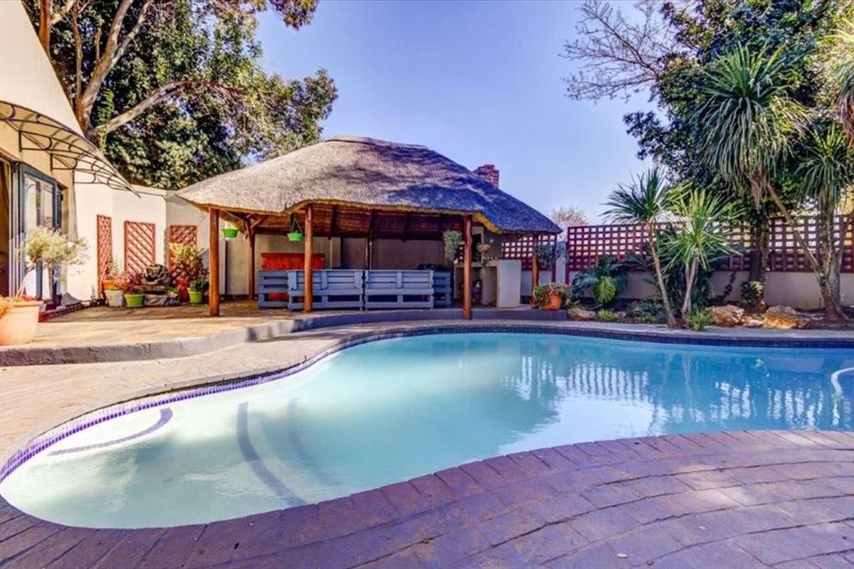 Outdoor entertainment area featuring a swimming pool and a covered thatch lapa with a built-in braai, set within a landscaped garden.