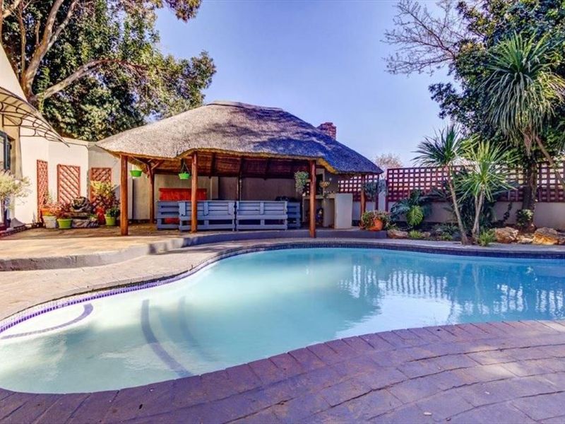 Outdoor entertainment area featuring a swimming pool and a covered thatch lapa with a built-in braai, set within a landscaped garden.