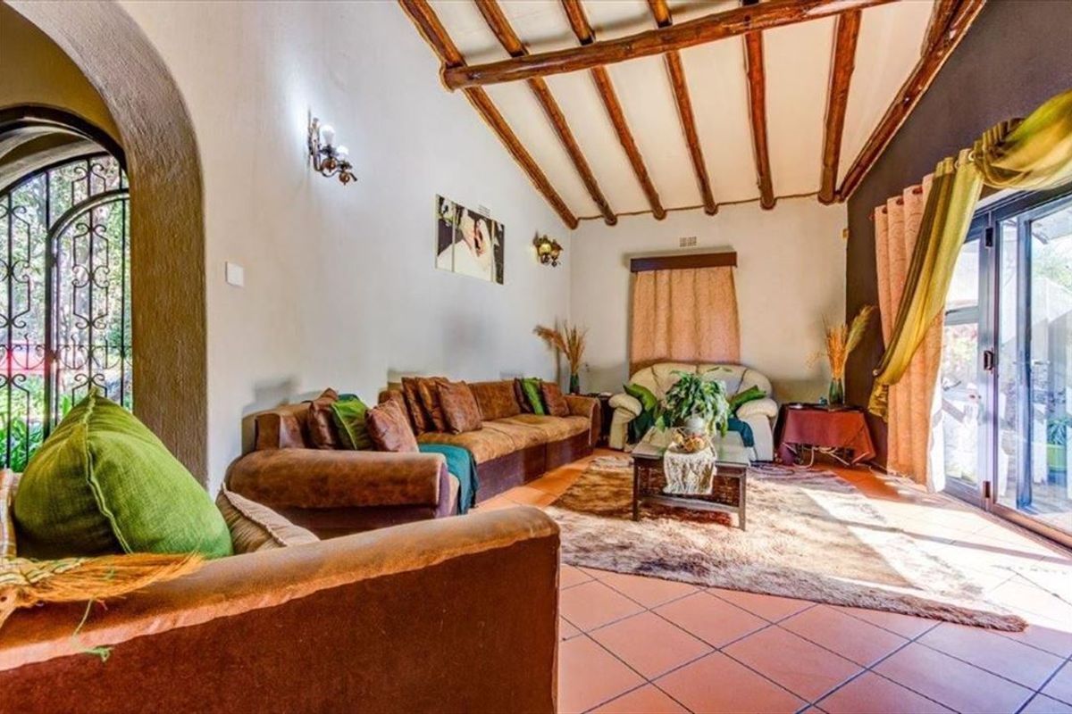 Spacious living room featuring exposed timber ceiling beams, terracotta-style tiled flooring, and large sliding glass doors providing access to the outdoor area.
