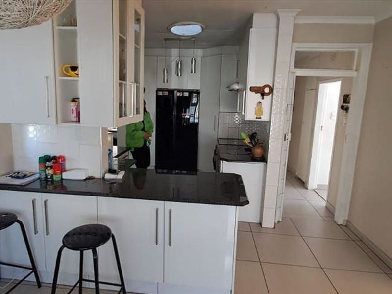A functional kitchen featuring white cabinetry, dark granite countertops, and tiled flooring, with an open-plan layout connecting to the adjacent hallway.