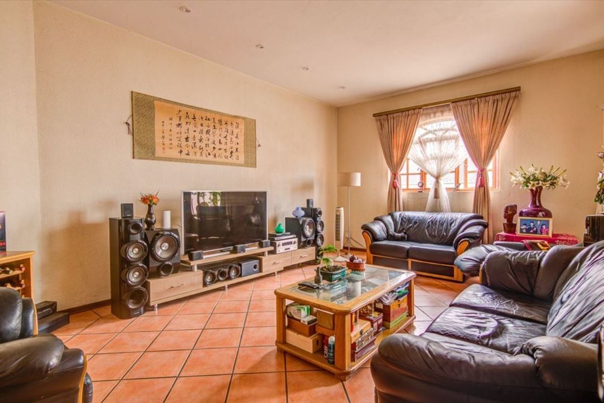 A spacious living room featuring terracotta floor tiles, recessed ceiling lighting, and a large window with curtain treatments.