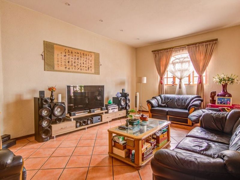 A spacious living room featuring terracotta floor tiles, recessed ceiling lighting, and a large window with curtain treatments.