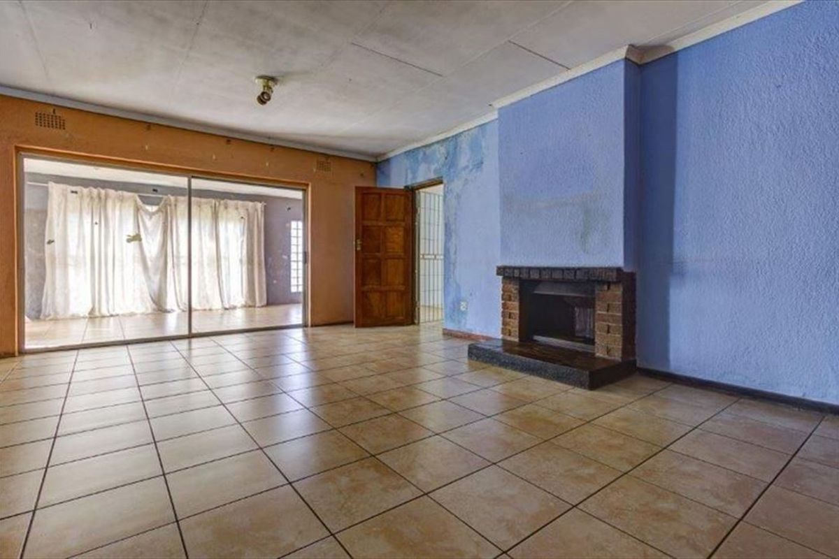 Spacious living room featuring tiled flooring, a brick fireplace, and sliding glass doors leading to an adjacent area, requiring cosmetic updates and wall repairs.