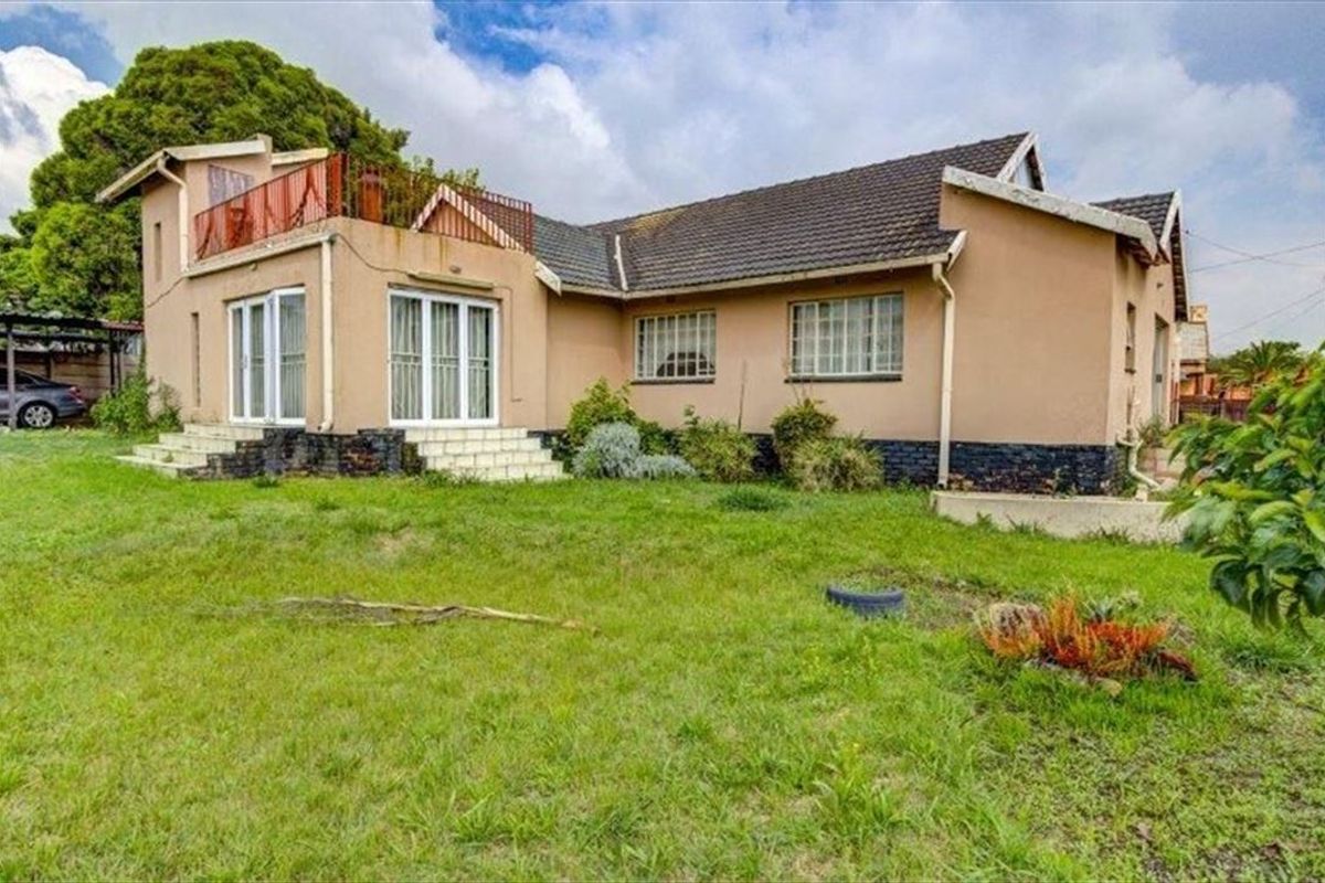 Rear view of the property featuring a tiled roof, upper-level balcony with metal railing, and sliding door access to the garden area.