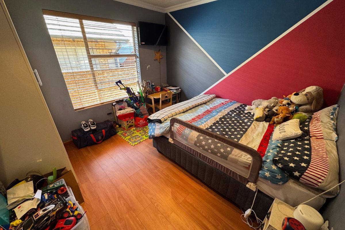 A bedroom featuring laminate flooring, built-in storage, and a window with venetian blinds, currently decorated with a geometric accent wall.