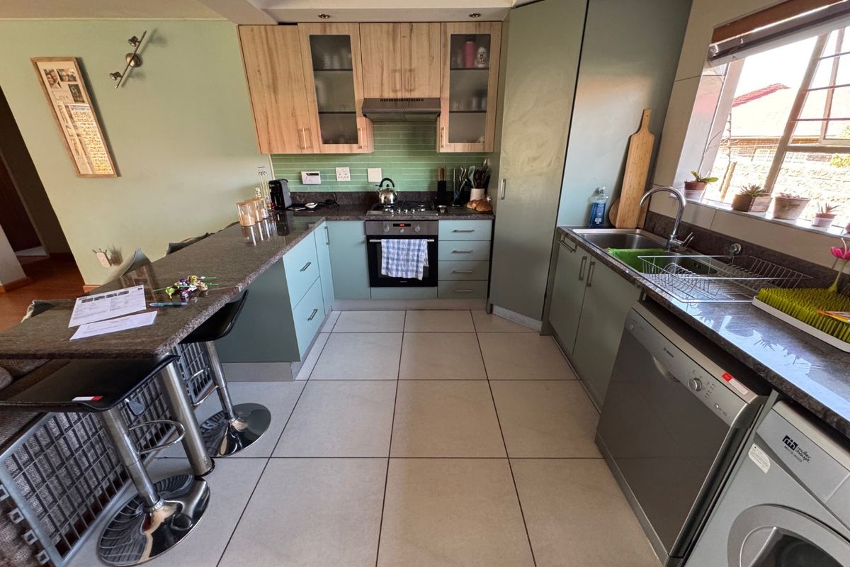 Functional kitchen featuring light wood and sage green cabinetry, granite countertops, integrated oven, gas hob, and tiled flooring with a breakfast bar.