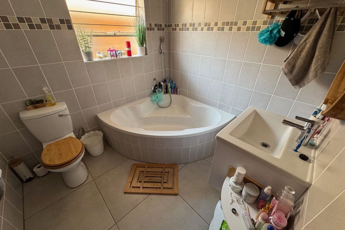 A functional bathroom featuring a corner bathtub, tiled walls and flooring, a vanity basin, and a toilet.