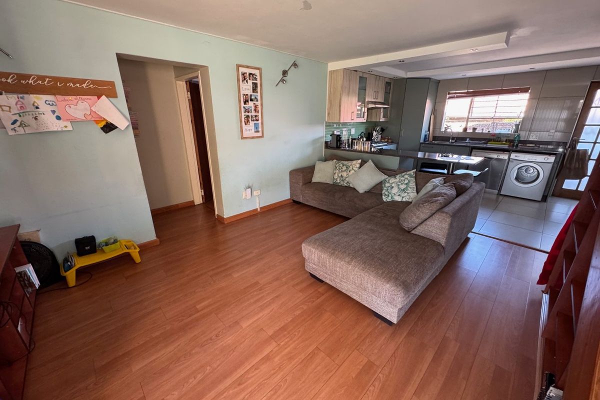 Open-plan living area featuring laminate flooring and a functional kitchen with built-in cabinetry, oven, and integrated laundry appliances.