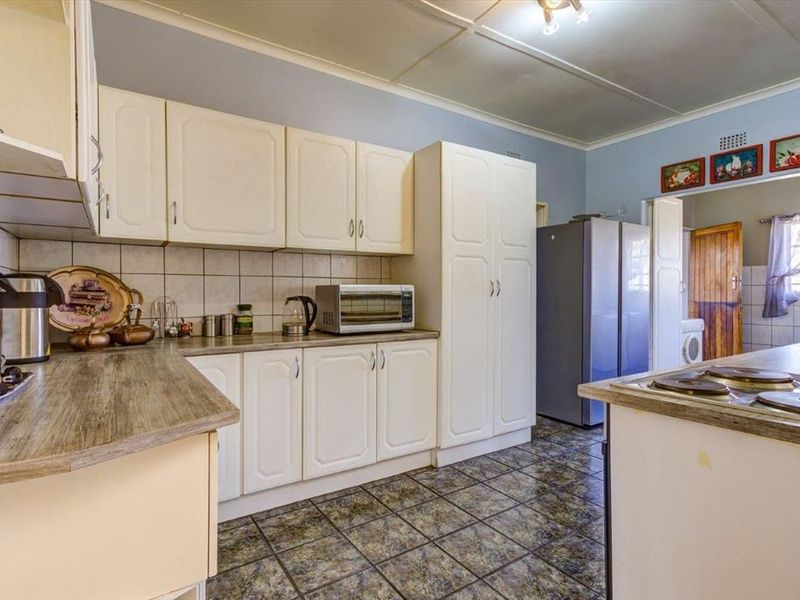 A functional kitchen featuring white built-in cabinetry, laminate countertops, tiled backsplash, and a built-in electric hob with adjacent pantry storage.