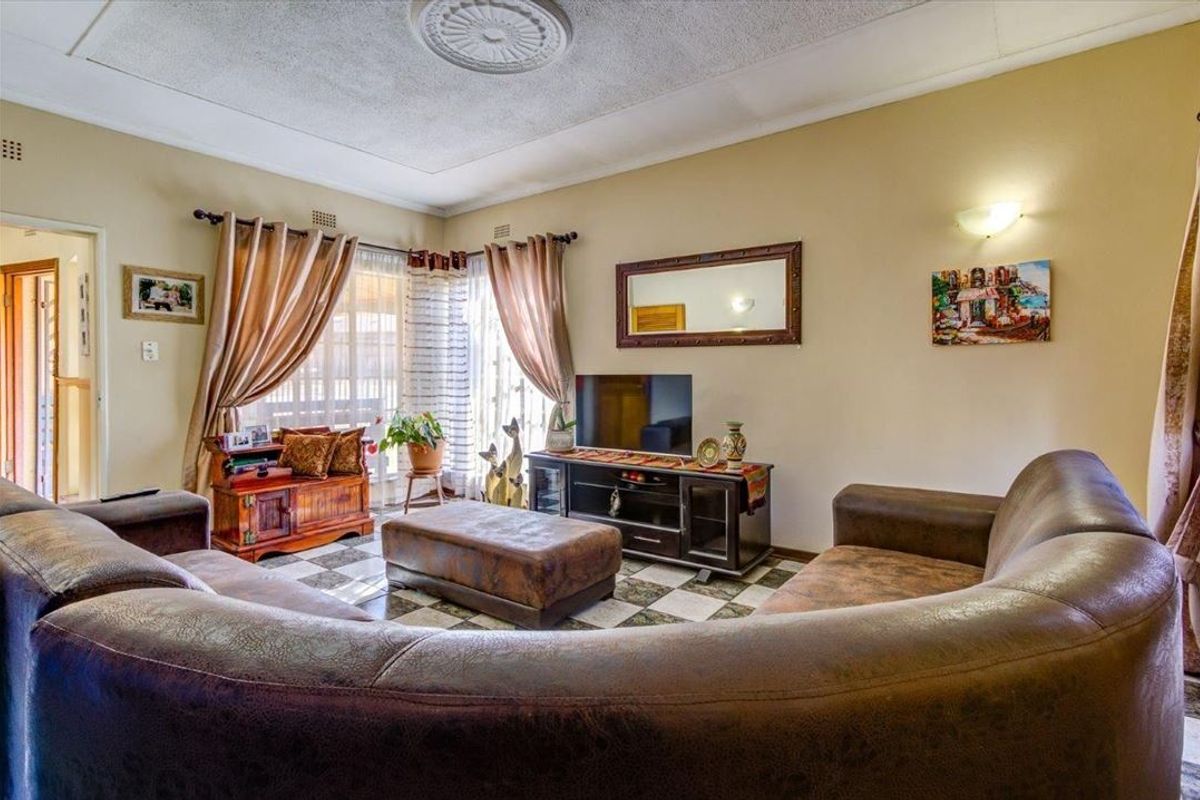 A living room featuring tiled flooring, a decorative ceiling rose, and wall sconce lighting, currently showing signs of wear and dated finishes.