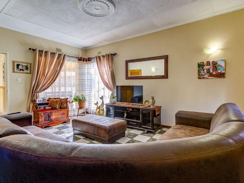 A living room featuring tiled flooring, a decorative ceiling rose, and wall sconce lighting, currently showing signs of wear and dated finishes.