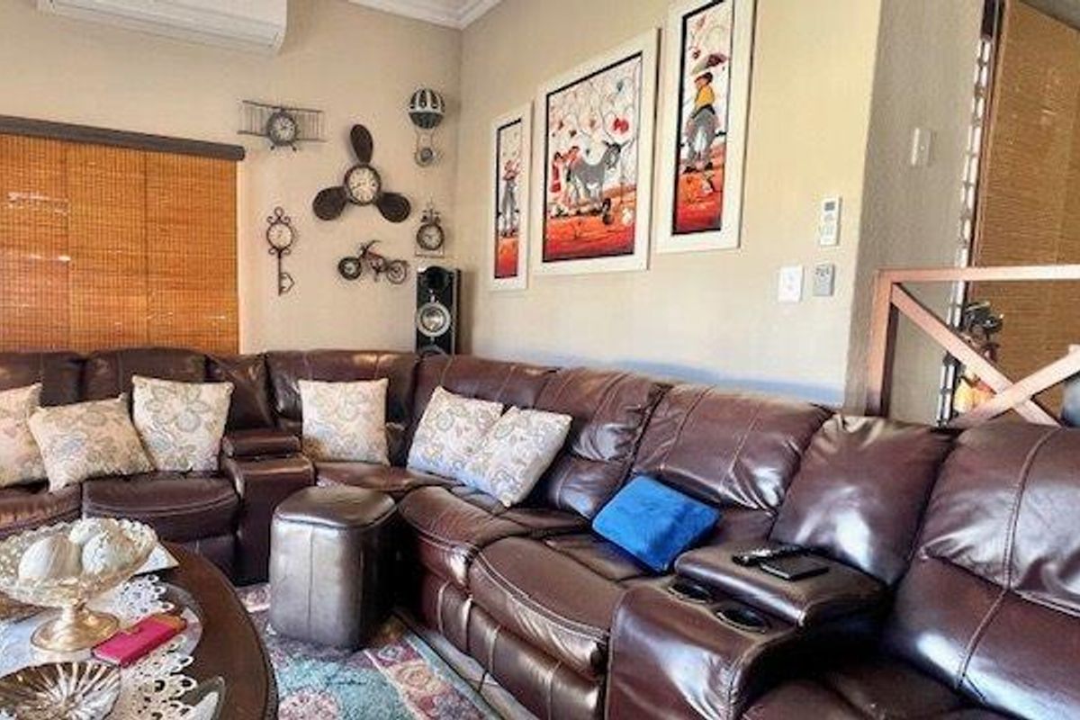 A comfortable living room featuring neutral walls, coving, bamboo blinds, and a wall-mounted air conditioning unit.