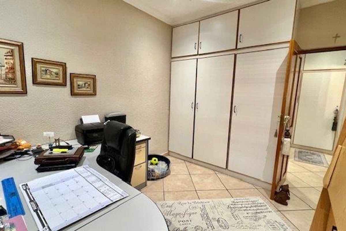 A bedroom featuring built-in cupboards with overhead storage and tiled flooring, currently utilized as a home office space.