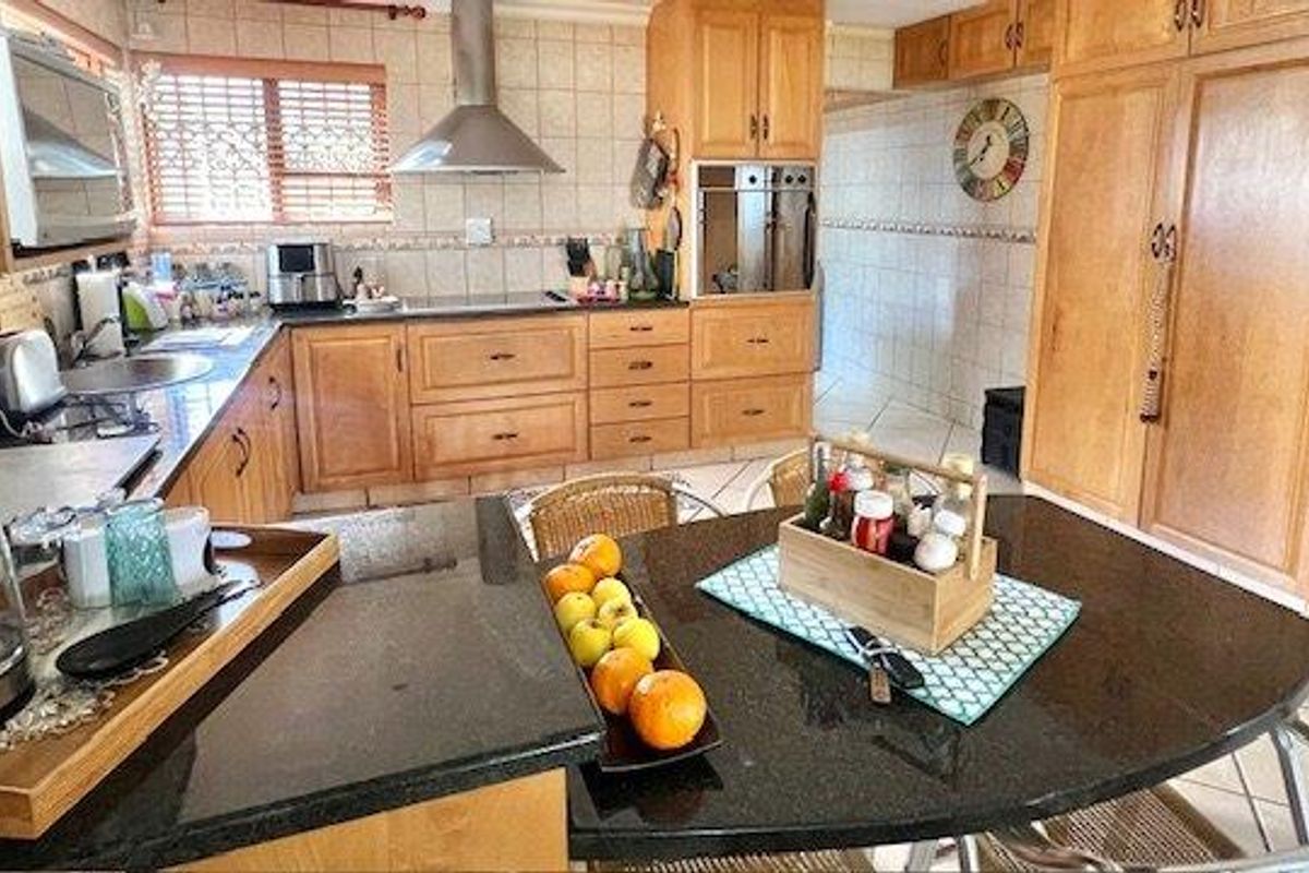A functional kitchen featuring wooden cabinetry, granite countertops, a built-in oven, and a stainless steel extractor fan with tiled finishes throughout.