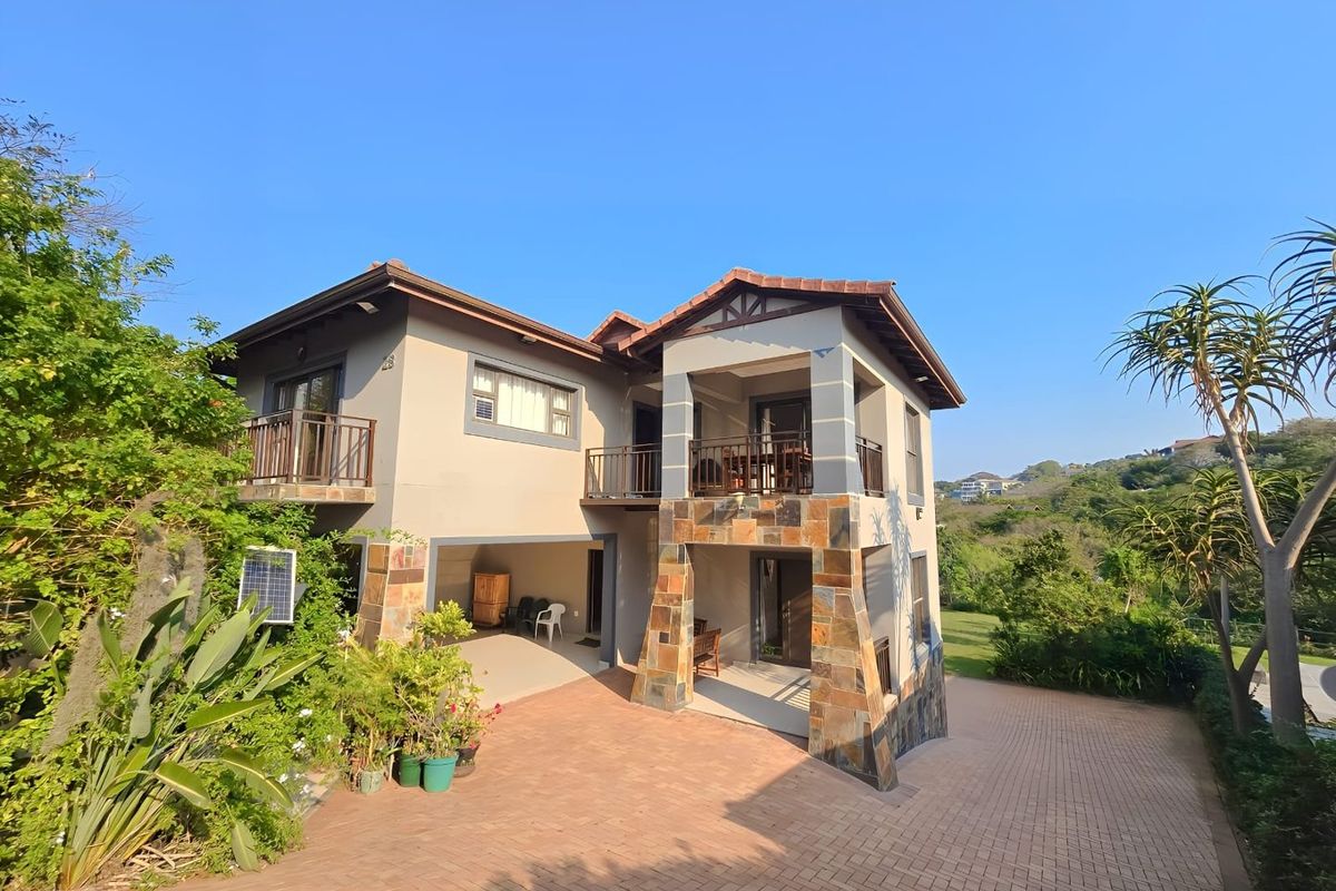 A multi-level residential property featuring stone-clad pillars, a paved driveway, and balconies overlooking a landscaped garden area.
