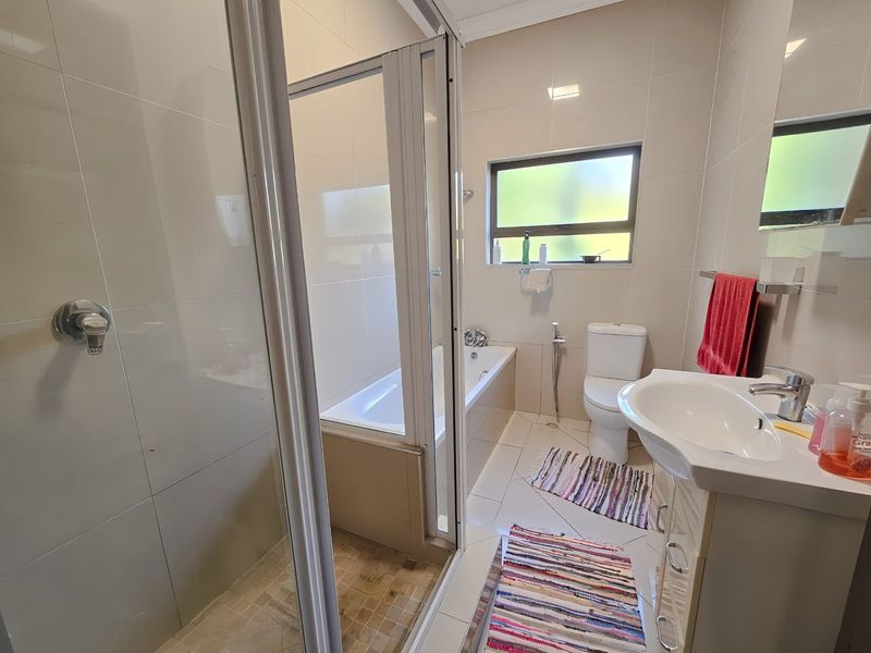 A functional bathroom featuring a glass shower enclosure, a built-in bathtub, a toilet, and a vanity basin with tiled finishes throughout.