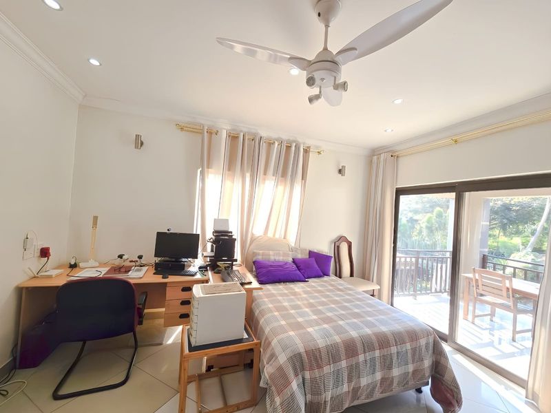A well-lit bedroom featuring tiled flooring, a ceiling fan, and large sliding glass doors that provide access to an outdoor balcony.