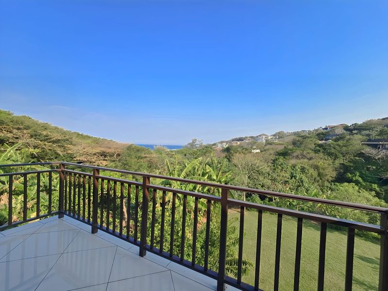 A spacious balcony featuring tiled flooring and a secure metal balustrade, offering expansive views of the surrounding landscape and distant coastline.