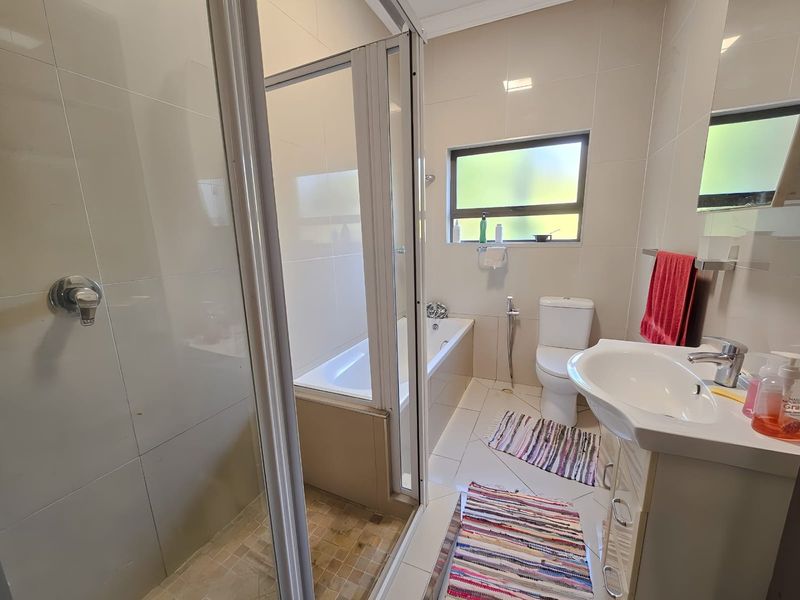 A functional bathroom featuring a shower enclosure, built-in bathtub, toilet, and vanity basin with neutral wall and floor tiling.