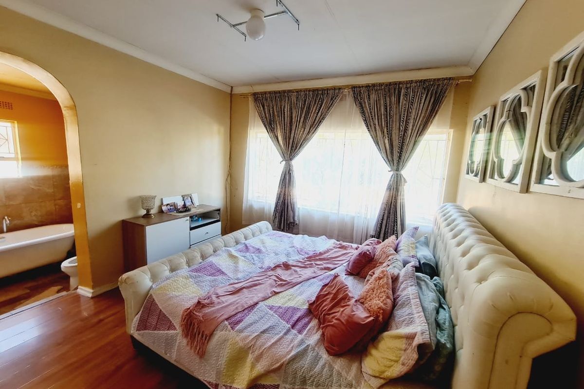 A bedroom featuring laminate flooring and an arched entryway leading to an en-suite bathroom, with window security bars and neutral wall tones.