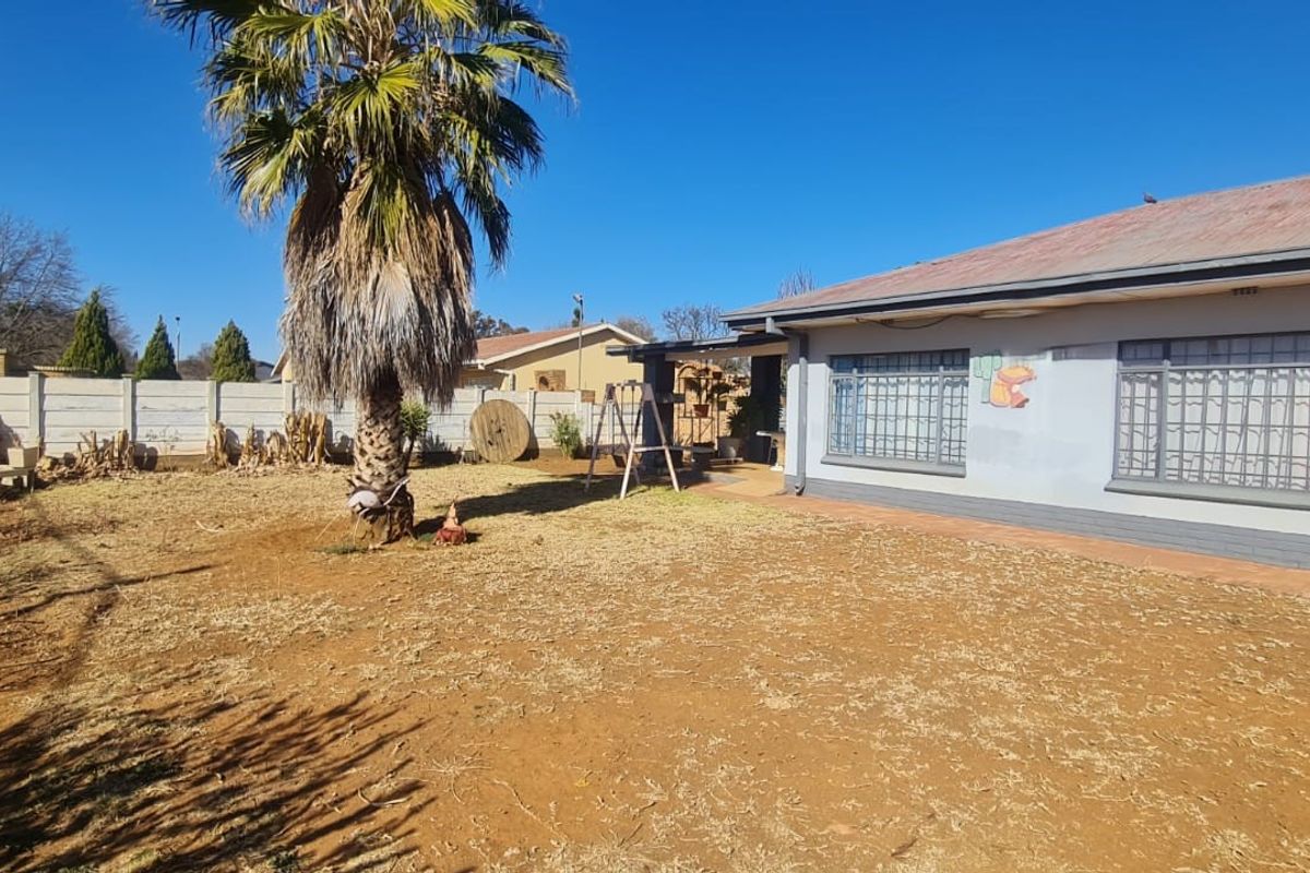Rear view of the property featuring a large garden, metal roof, and security bars on the windows.