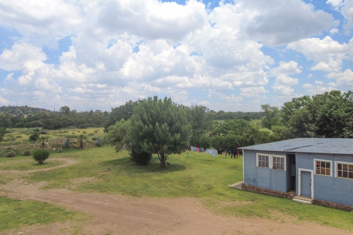 An elevated view of the rear of a farm building featuring painted brick walls and a corrugated metal roof set within a large rural landscape.