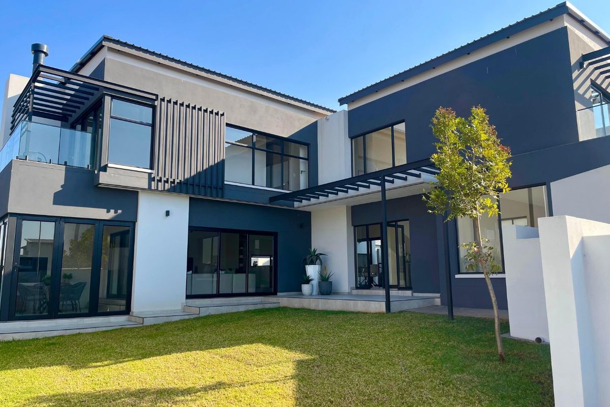 Modern double-story rear elevation featuring dark grey and white facade, glass balustrades, covered patio areas, and a well-maintained lawn.