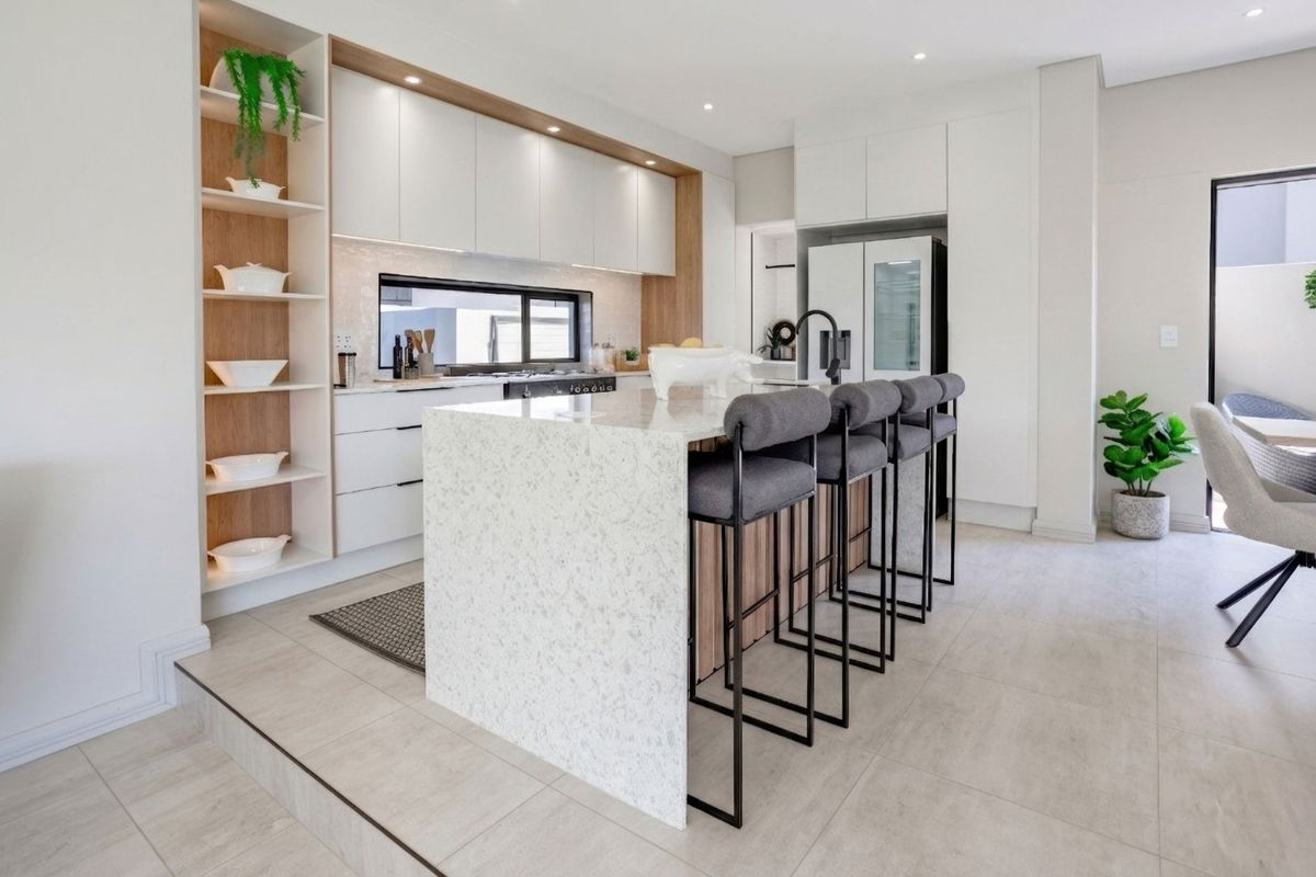 Modern kitchen featuring a stone island, sleek white cabinetry, integrated shelving, and high-quality finishes in an open-plan layout.