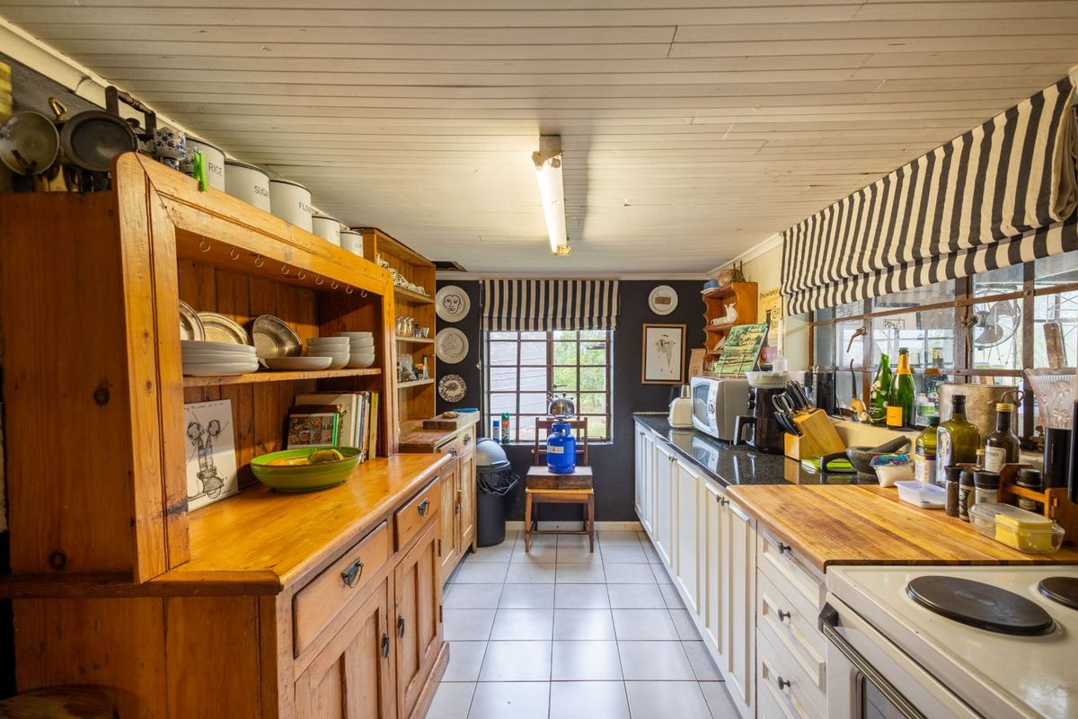 A rustic farmhouse kitchen featuring a mix of wooden cabinetry, granite and butcher block countertops, tiled flooring, and a timber plank ceiling.