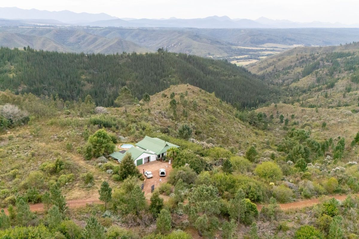 Aerial view of a farm property nestled in a mountainous landscape, featuring a main dwelling with a metal roof and a private swimming pool.