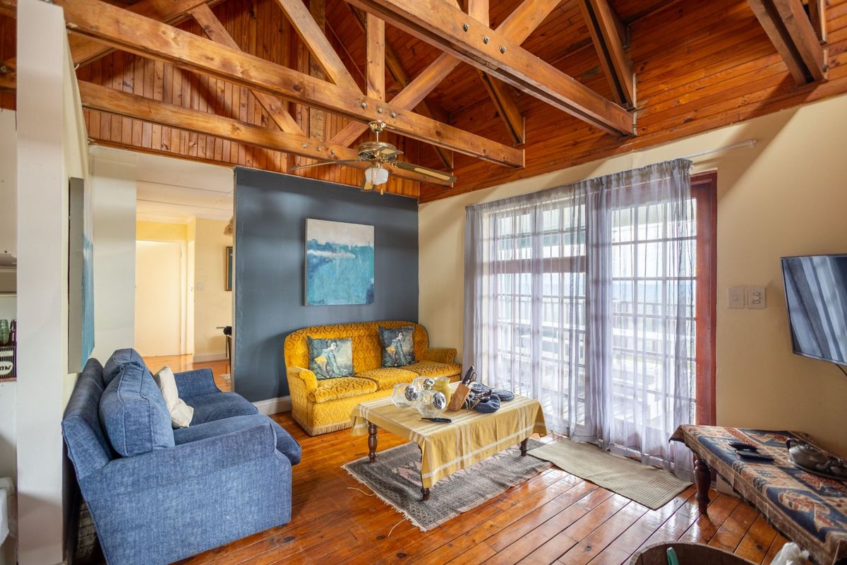 A cozy living room featuring exposed timber roof trusses, warm wood flooring, and a sliding glass door providing natural light and access to the exterior.