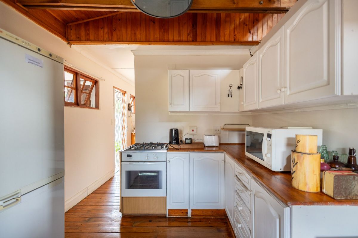 A functional kitchen featuring white cabinetry, wooden countertops, a gas stove, and a rustic timber ceiling with matching wooden flooring.