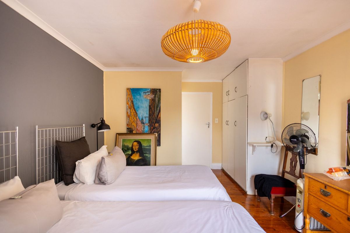 A bedroom featuring hardwood flooring, built-in cupboards, and a pendant light fixture, offering a functional space with neutral wall tones.