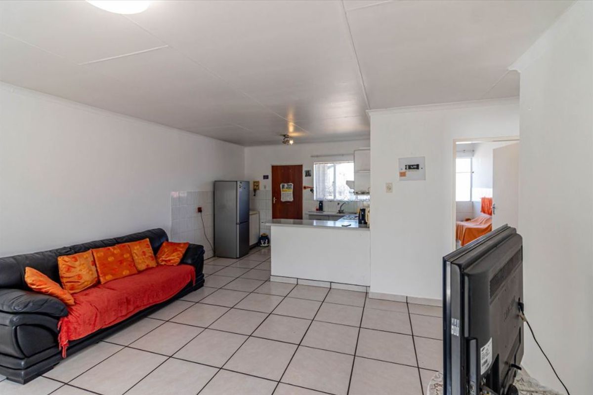 Open-plan living area featuring tiled flooring and a functional kitchen with a breakfast bar, providing a practical and connected living space.