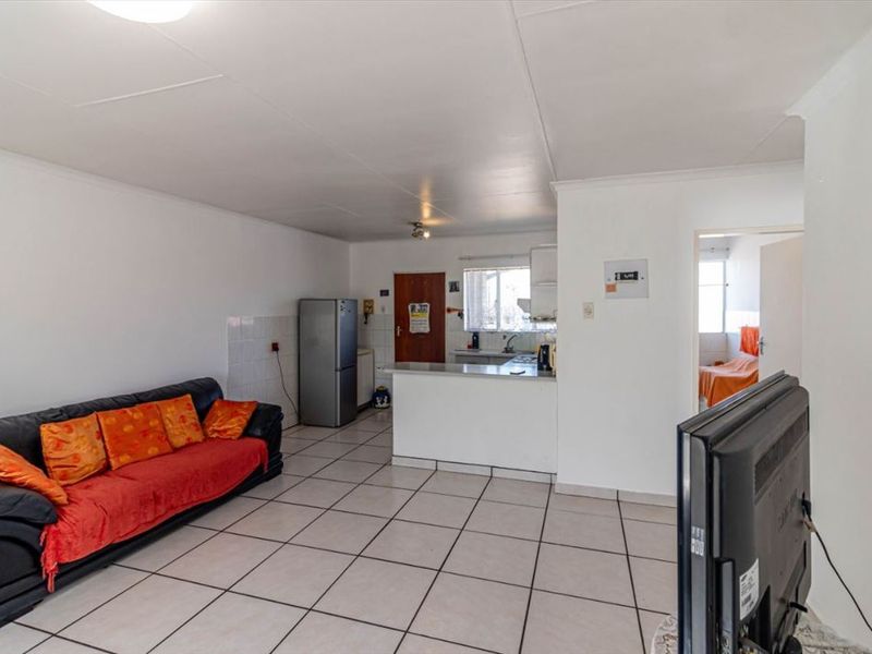 Open-plan living area featuring tiled flooring and a functional kitchen with a breakfast bar, providing a practical and connected living space.