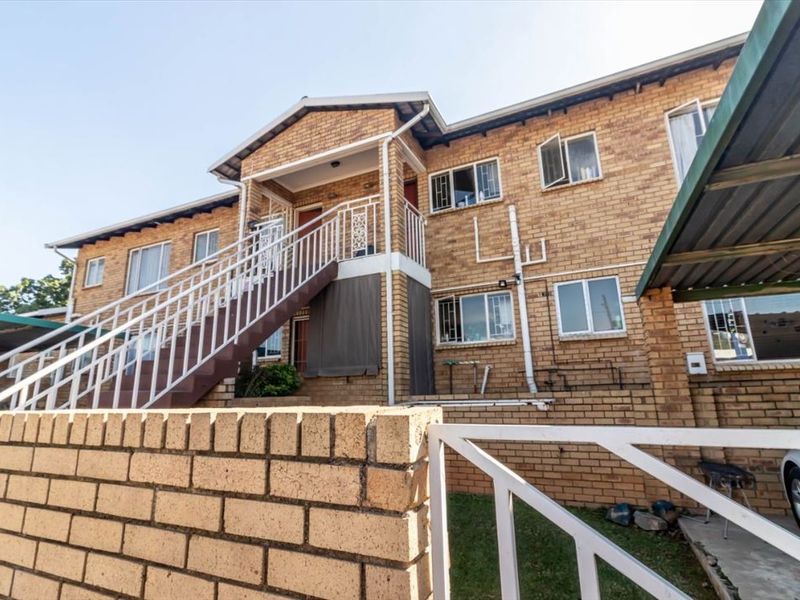 Exterior view of a multi-level townhouse complex featuring face-brick construction, an external staircase, and dedicated carport parking.