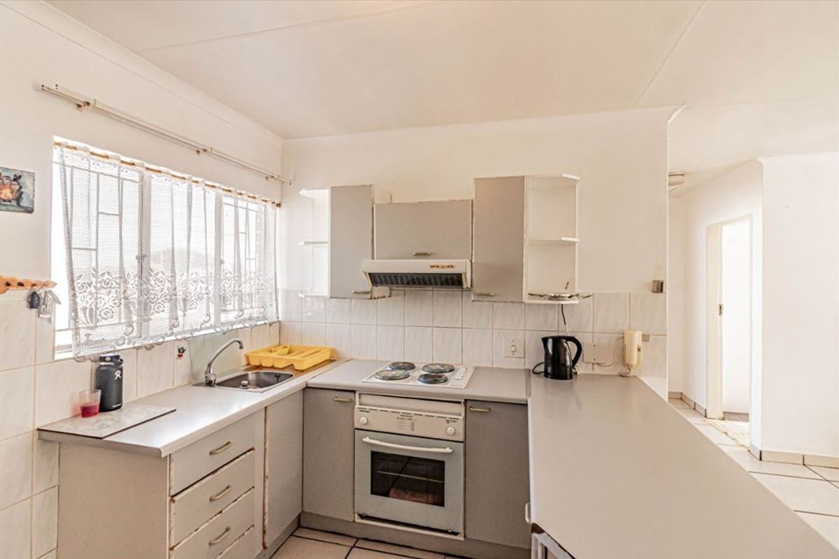 A functional kitchen featuring built-in cabinetry, laminate countertops, an electric hob, oven, and tiled backsplash with natural light from the window.