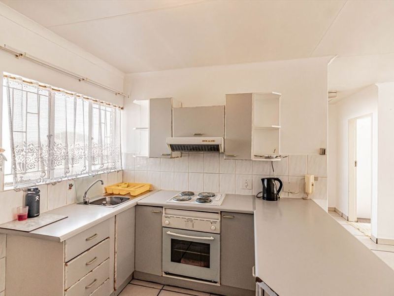 A functional kitchen featuring built-in cabinetry, laminate countertops, an electric hob, oven, and tiled backsplash with natural light from the window.