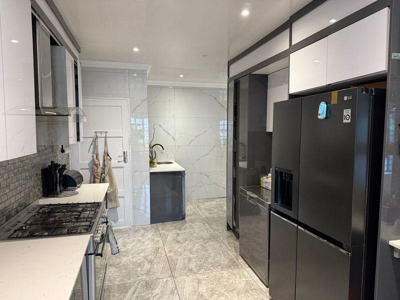 Modern kitchen featuring high-gloss cabinetry, stone countertops, marble-look wall tiling, and integrated gas hob with extractor fan.