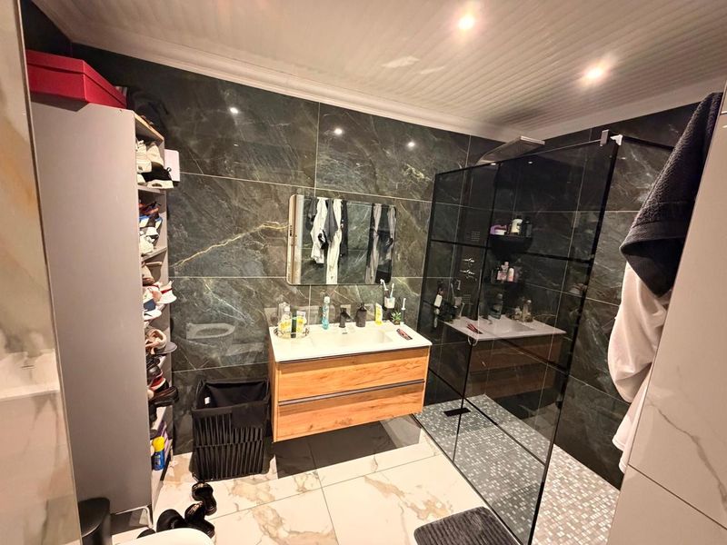 Modern bathroom featuring dark marble-effect wall tiles, a floating wood-finish vanity, and a spacious walk-in shower with a glass enclosure.