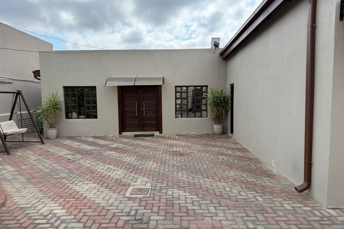 A paved rear courtyard area featuring a double wooden entrance door, modern awning, and clean exterior wall finishes.