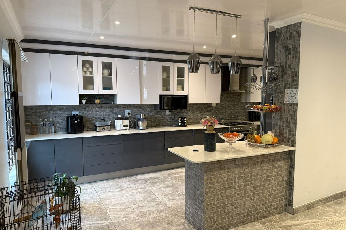 Modern kitchen featuring two-tone cabinetry, stone countertops, a central island with pendant lighting, and a decorative stone tile backsplash.
