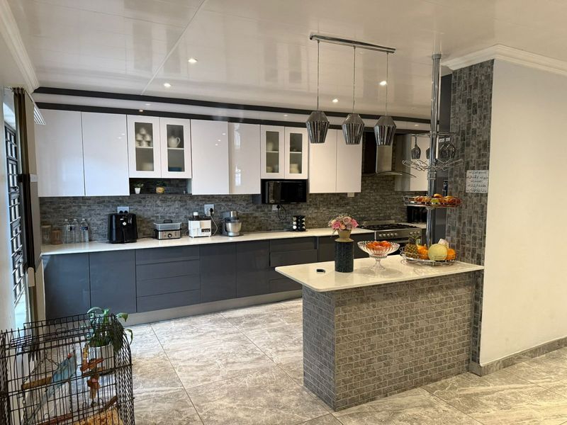 Modern kitchen featuring two-tone cabinetry, stone countertops, a central island with pendant lighting, and a decorative stone tile backsplash.